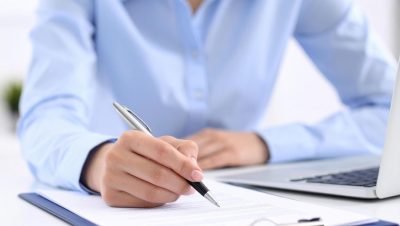 69855549-pessoa-escrevendo-em-documento-com-caneta-enquanto-sentado-as-escrivaninha-com-computador-portatil-proximo-exibindo-foco-e-produtividade-gratis-foto